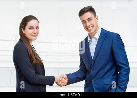 Close up portrait of young business couple habillés en costumes se serrer la main avec en arrière-plan du bureau. Banque D'Images