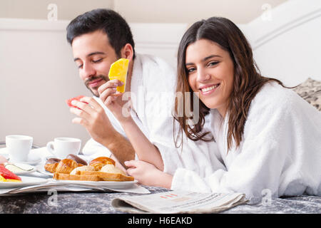 Close up portrait of couple having breakfast together on bed in hotel room.Couple wearing peignoirs. Banque D'Images