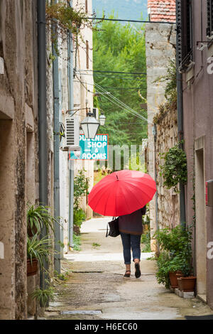 Une femme portant un parapluie rouge vif dans une petite ruelle de Ston en Croatie sous un ciel couvert et journée de bruine Banque D'Images