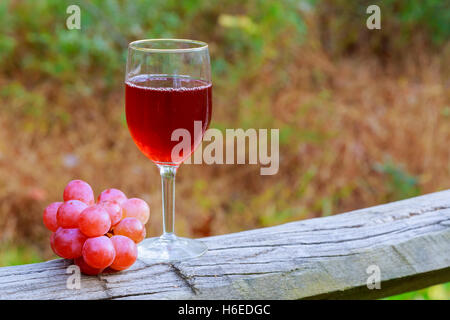 Verre à vin rouge et grappe de raisins sur table en bois contre le vignoble en été Banque D'Images