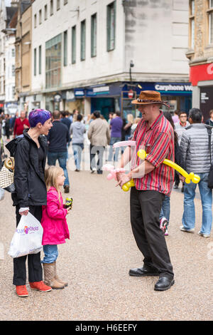 Un artiste de rue divertit une petite fille et sa mère avec des ballons sur Cornmarket Street, Oxford, Royaume-Uni Banque D'Images