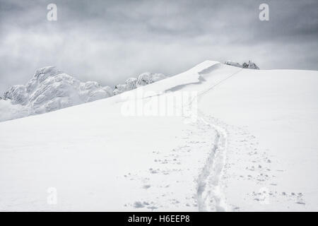 Une piste de ski mène de l'avant-plan vers le haut d'une montagne sur une journée nuageuse. Banque D'Images