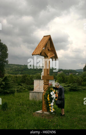 Vieille Femme priant au crucifix en bois posées à la mémoire des victimes du communisme de Sighet, Roumanie Banque D'Images