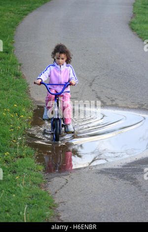 Little girl riding a bike avec roues de formation par flaque sur le sentier Banque D'Images