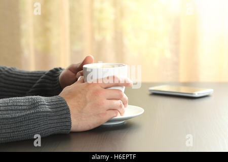 Close-up of a man holding relaxant mains une tasse de café dans une table en bois à la maison avec une fenêtre à l'arrière-plan Banque D'Images