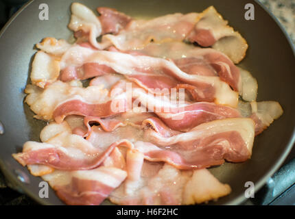 Bacon de porc cru être frit dans une casserole en téflon Close Up Banque D'Images