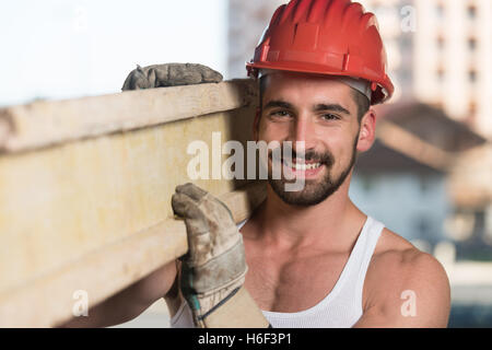 Smiling Carpenter transporte une grande planche en bois sur son épaule Banque D'Images