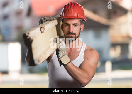 Smiling Carpenter transporte une grande planche en bois sur son épaule Banque D'Images
