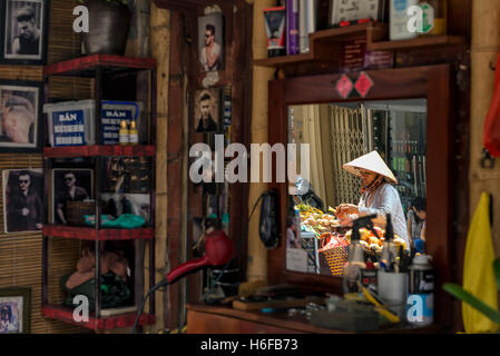 Réflexion d'un vendeur de fruits sur le miroir d'une boutique de coiffeur dans une rue de Hanoi. Banque D'Images