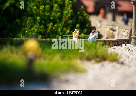 Petites figurines de famille assis sur un banc dans le jardin. Banque D'Images