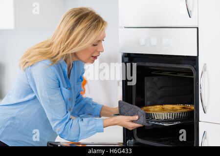 Jolie blonde woman putting tart dans le four pour la cuisson Banque D'Images