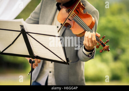 Violoniste mâle jouant son instrument et la lecture d'une feuille de musique pendant une cérémonie de mariage en plein air (shallow DOF ; couleur à Banque D'Images
