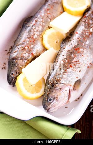 Photo verticale de deux matières truites. Poissons en céramique bleu pan sur planche de bois avec une serviette verte autour. Herbes comme le thym et rosemar Banque D'Images