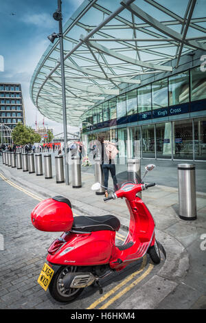 Londres, Angleterre, Royaume-Uni : un transport ferroviaire des passagers arrivant à King's Cross station sur un scooter Vespa rouge Banque D'Images