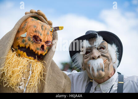 Merrick, New York, USA. 29 Oct, 2016. À droite, Jim Johnson, du Merrick portant un costume de Munchkin Wizard of Oz, se tient devant sa cour décorée dans un effrayant spooky Wizard of Oz thème, à divertir les gens comme ils marchent dans la rue à l'entrée de parc Fraser pour l'année 2016 Grimaces dans Merrick a accueilli en partie par le nord et le centre de l'Association civique Merrick (NCMCA). JOHNSON'S main reposait sur un homme de paille horrible, macabre décoration pelouse, avec un daggner plongé dans sa tête de citrouille. © Ann Parry/ZUMA/Alamy Fil Live News Banque D'Images