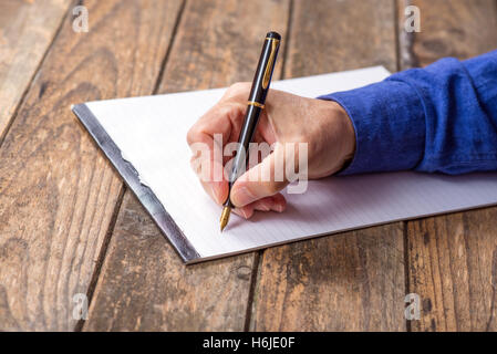 La main de l'homme écrit avec un stylo à fond de bois. Banque D'Images