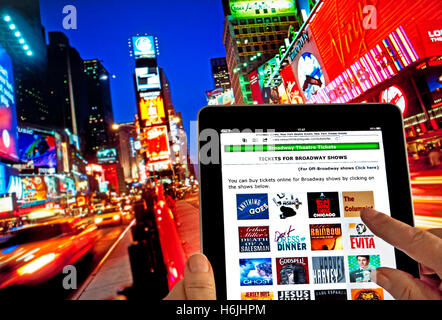 Concept image of hand holding Tablet computer at Dusk with finger touching screen displaying live en ligne Achat de billet pour les spectacles de théâtre de Broadway Times Square New York USA Banque D'Images