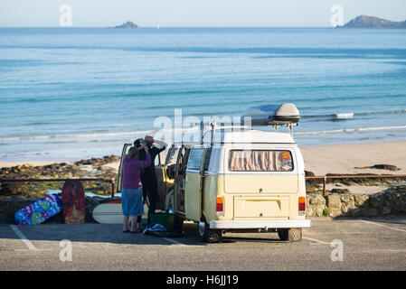 Les surfeurs à un vintage Volkswagen bus camping préparer une combinaison isothermique pour une matinée de surf à Sennen Cove au début de la matinée, Cornwall, UK Banque D'Images