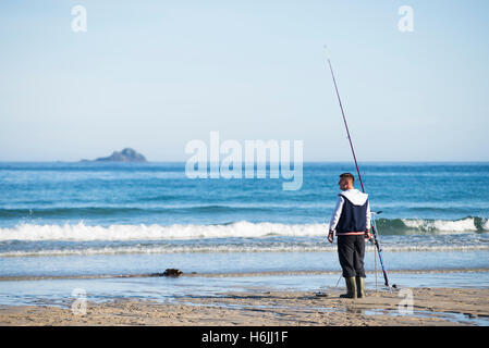 Pêcheur sur la plage de Sennen Cove en face d'une île à l'horizon de l'Océan Atlantique après le lever du soleil, Cornwall, Angleterre, Royaume-Uni Banque D'Images