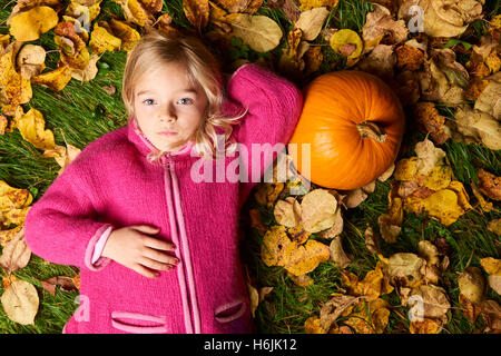 Enfant mignon fille blonde allongée dans les feuilles d'automne à la citrouille. Banque D'Images