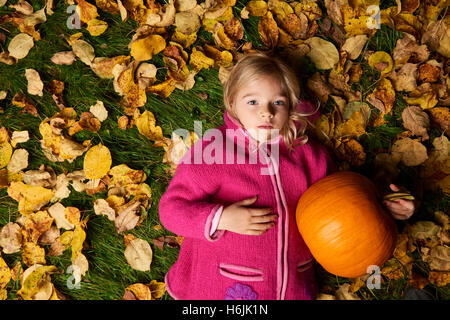 Enfant mignon fille blonde allongée dans les feuilles d'automne à la citrouille. Banque D'Images