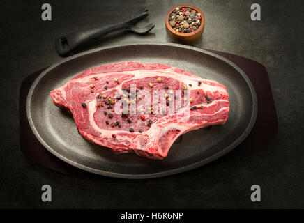 Moody et sombre image d'un steak cru organique sur une plaque de fer pour la cuisson avec du poivre en grains Banque D'Images