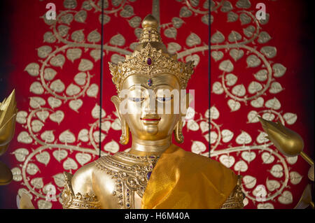 Golden buddha avec sash close up contre un arrière-plan à motifs floraux décoratifs lumineux dans un temple bouddhiste, Bangkok, Thaïlande Banque D'Images