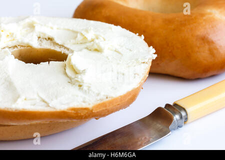 Bagel nature avec couteau, tartiner avec du fromage à la crème, détail. Banque D'Images