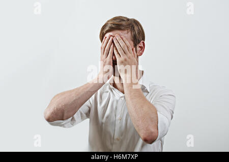 Les jeunes adultes de sexe masculin portant chemise blanche couvre son visage par les deux mains, faisant des gestes qu'il a fait une grosse erreur Banque D'Images