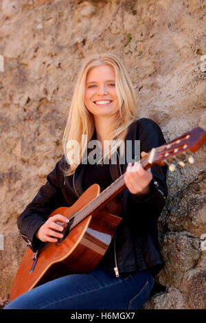 Cool blonde girl playing guitar appuyé contre un mur de pierre Banque D'Images