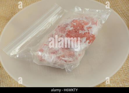 Deux pâtés de bœuf décongélation dans un sac plastique sur la plaque blanche Banque D'Images