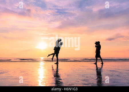 Photographe de prendre une photo d'un couple sur la plage pendant le coucher du soleil - concept à propos de miel et voyages romantiques Banque D'Images