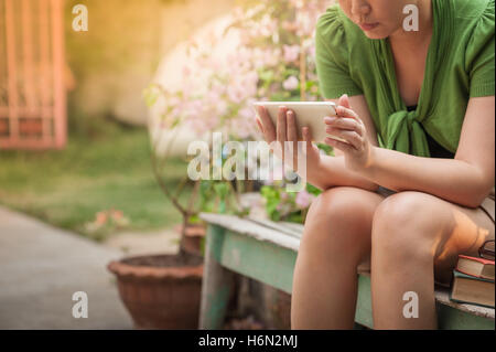 Scène de vie matin de jeunes hipster woman using mobile phone alors qu'il était assis sur un banc en bois. avec tec numérique Banque D'Images