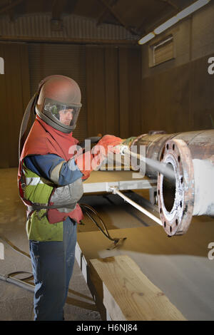 Un travailleur utilise grit haute pression sablage pour nettoyer une section de tuyau de raffinerie à une installation de maintenance pétrochimique Banque D'Images