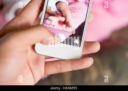 Mère using smartphone prendre une photo de son bébé. Photo de bébé est une des plus populaires dans les réseaux sociaux Banque D'Images