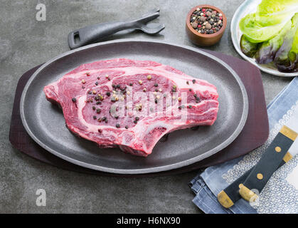 Délicieux boeuf cru organique sur une plaque de fer avec plaque de cuisson poivre corns en attente sur un barbecue Banque D'Images