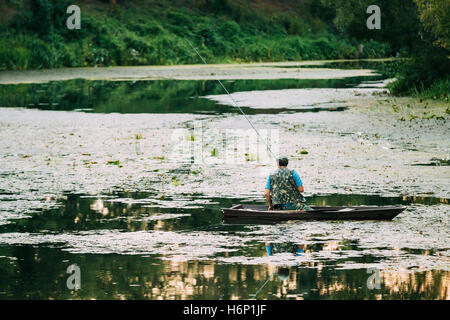 Lone Man Fish-Rod Pêcheur, assis dans une petite barque en bois vert dans la rivière étang envahi par la mare en été. Banque D'Images