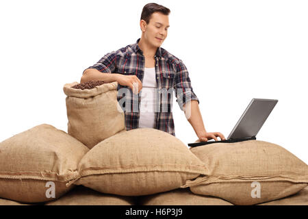 Travailleur agricole posant avec sacs de toile remplis de grains de café et de travailler sur un ordinateur portable isolé sur fond blanc Banque D'Images