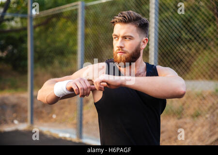 Portrait si un beau jeune sportif barbu mains étirement lors de l'entraînement à l'extérieur Banque D'Images