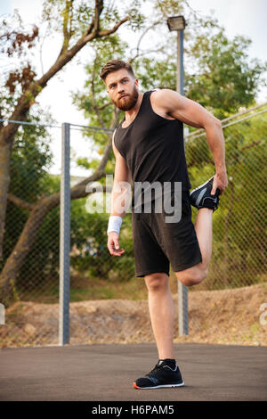 Portrait of a handsome sportsman barbu qui s'étend à l'extérieur des jambes Banque D'Images