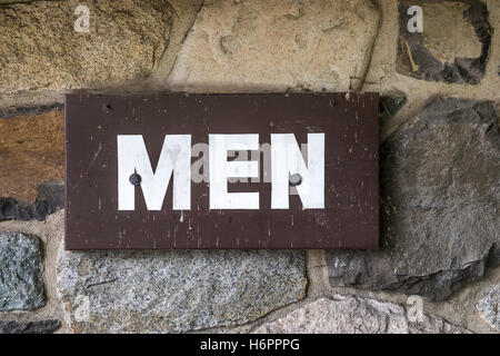 Un signe d'hommes peints sur bois est suspendu sur un mur de pierre à l'extérieur d'une toilette. Banque D'Images