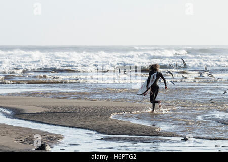 Surfer running on beach with surfboard à Saltburn by the sea, North Yorkshire, Angleterre, Royaume-Uni. Banque D'Images