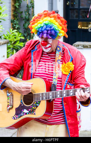 Un clown dans une perruque arc-en-ciel et veste rouge à jouer de la guitare à une fête de quartier dans le nord de Londres, UK Banque D'Images