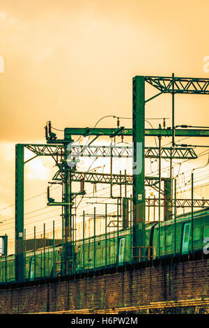 Ciel jaune au coucher du soleil plus de portiques et de fils électriques sur la ligne de chemin de fer hors de St Pancras International Station, London, UK, un train, 2012 Banque D'Images