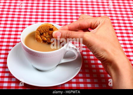 Femme-chers-filles part tremper un biscuit cookie dans d'une tasse de thé chaud avec une croix rouge et blanc tissu table vérifiées Banque D'Images