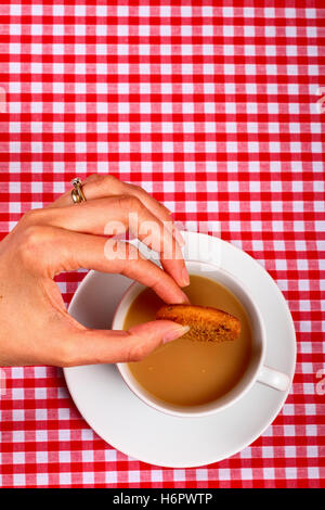 Femme-chers-filles part tremper un biscuit cookie dans d'une tasse de thé chaud avec une croix rouge et blanc tissu table vérifiées Banque D'Images