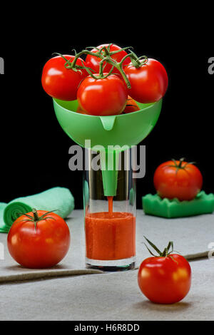 Les tomates dans un entonnoir en verre avec du jus de tomate Banque D'Images