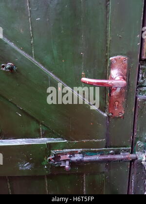 Une poignée en métal peint en rouge, et le verrou sur une porte en bois vert. Banque D'Images