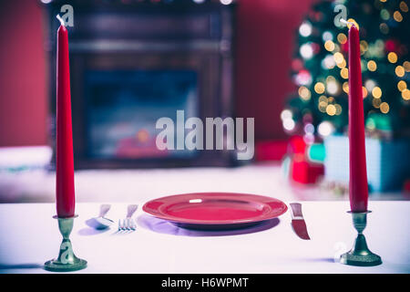 Nouvelle année magnifiquement mis à table avec des assiettes et des couverts rouges sur fond d'arbre de Noël décoré avec cheminée et Banque D'Images