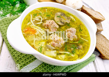 Soupe avec des boulettes de viande, les nouilles et les champignons dans un bol blanc sur une serviette vert, le persil sur un fond en bois Banque D'Images